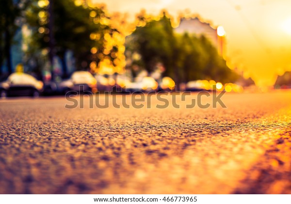 Sunset in the city, the road with parked cars.\
Close up view from the level of the dividing line, image in the\
orange-purple toning