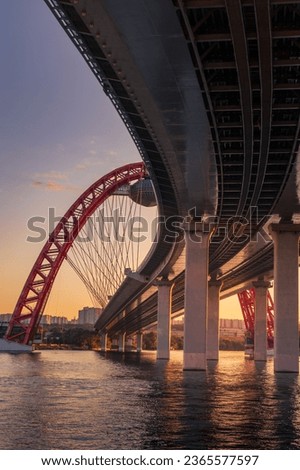 Sunset cityscape with modern arched cable stayed bridge reflecting in a river water against a colorful sky, Moscow, Russia