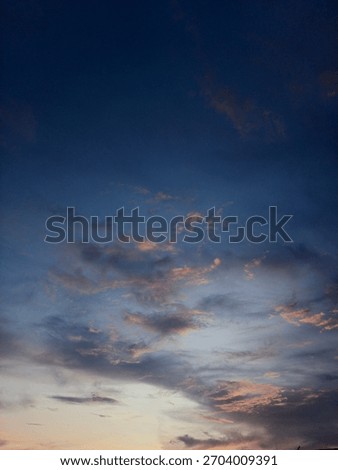 ​Dramatic sunset clouds fill a deep twilight sky, highlighted by streaks of orange and pink light near the horizon.The dark,intense blue dominates the upper frame,creating a striking moody atmosphere.