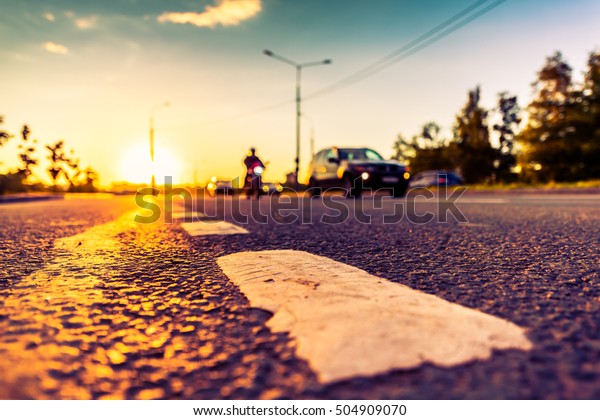 Sunset in the country, the bike and\
cars driving on the highway. Wide angle view of the level of the\
dividing line, image in the orange-purple\
toning