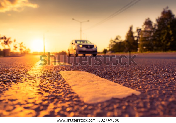 Sunset in the country, the car on the highway.\
Wide angle view of the level of the dividing line, image in the\
soft orange-purple\
toning