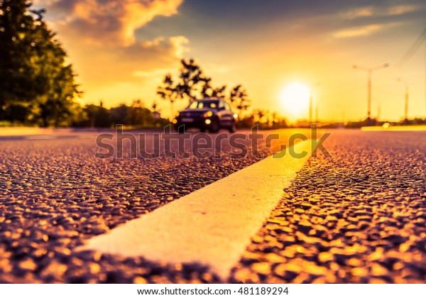 Sunset in the country, the car rides on the\
highway. Wide angle view of the level of the dividing line, image\
in the orange-purple\
toning