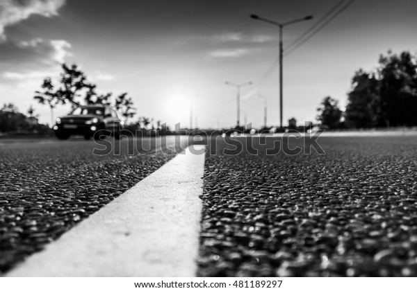 Sunset in the country, the car rides on the\
highway. Wide angle view of the level of the dividing line, image\
in the black and white\
tones