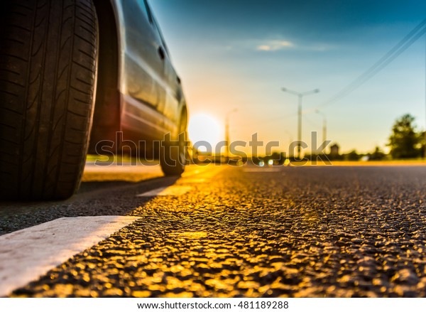 Sunset in the\
country, the headlights of the approaching cars. Wide angle view of\
the level of a parked car\
wheels