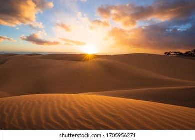 Sunset in the desert, sun and sun rays, Beautiful clouds on blue sky. Golden sand dunes in desert in Maspalomas, Gran Canaria, Canary islands, Spain
