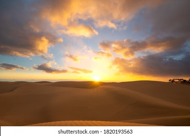 Sunset in the desert, sun and sun rays, dramatic colorful clouds in the sky. Golden sand dunes in desert in Maspalomas, Gran Canaria, Canary islands, Spain.