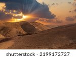 Sunset in the desert and sun rays spreading. Beautiful dramatic clouds on gold sky. Golden sand dunes in desert in Judean desert, Israel. Sunny sky over cliffs, large salt mountains Sodom and Gomorrah