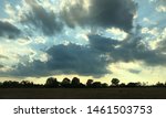 Sunset with dramatic rays of light and cloud formations over farmland and deciduous trees in rural Virginia.