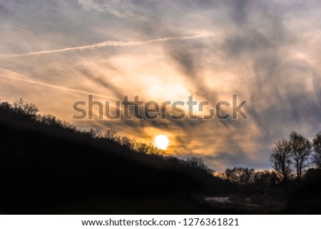 Sunset with dramatic sky with clouds and silhouettes of trees