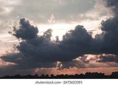 Sunset in a dramatic sky with the rays of a dream piercing through the dark clouds against the background of the city. Bright epic sky. Dramatic evening light and fiery orange sunset.