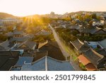 Sunset drapes over Jeonju Hanok Village, silhouetting traditional houses against a twilight sky, as a bustling street comes alive under the warm, atmospheric light.