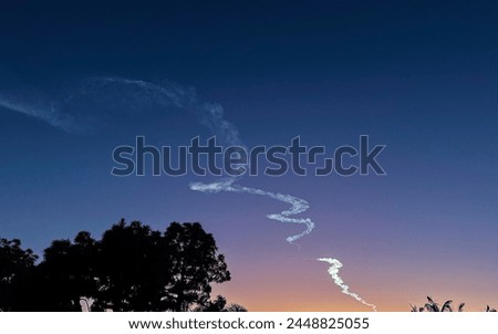 Sunset and dusk highlighting a rocket launch contrail with trees in contrast.