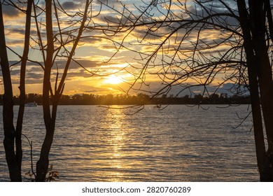 Sunset framed by bare tree branches over a shimmering lake or river