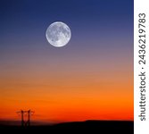 Sunset and Full Moon in sky in landscape with power lines on horion