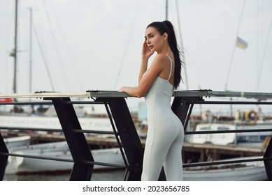 at sunset, a girl in a tight sports leotard in gray is standing on the pier.