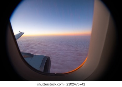 sunset horizon view from window seat in airplane in flight flying high above the purple fluffy clouds airplane wing and window frame in sight horizontal format room for type framed area air travel  - Powered by Shutterstock