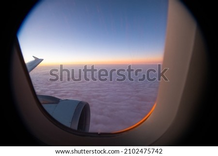 sunset horizon view from window seat in airplane in flight flying high above the purple fluffy clouds airplane wing and window frame in sight horizontal format room for type framed area air travel 