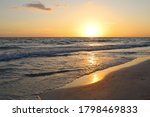 Sunset illuminates tranquil waves and shoreline along the beach in Lido Key off Sarasota, Florida. Glowing yellow sun sets over calm Gulf of Mexico waters near Siesta Key. Summer nights in FL.