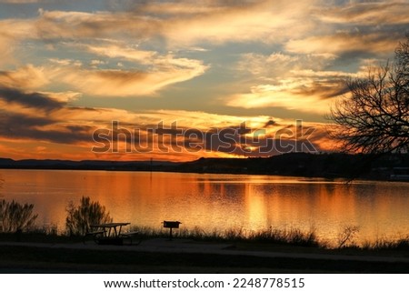 Sunset at Inks Lake State Park Burnet Texas USA. A picnic table and BBQ grill overlook the beautiful golden sunset-colored lake.