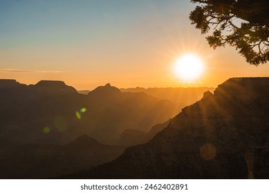 Sunset landscape with rugged mountains fading into distance, warm golden glow in the sky. Silhouetted tree branch frames the scene, lens flares add interest. Peaceful, majestic mood. - Powered by Shutterstock