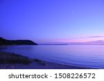 Sunset in Leland, Michigan along the Lake Michigan beach. Next to Falling Waters Lodge, near the municipal harbor the sun sets below a clear, blue sky with the moon coming into view.