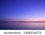 Sunset in Leland, Michigan along the Lake Michigan beach. Next to Falling Waters Lodge, near the municipal harbor the sun sets below a clear, blue sky with the moon coming into view.