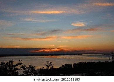 Sunset light creating orange and blue hues over a calm lake with silhouetted trees