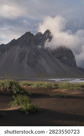 Sunset light filtering through clouds over black sand dunes and Vestrahorn mountain range at Stokksnes - Iceland