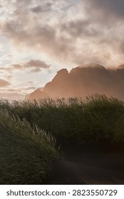 Sunset light filtering through clouds over black sand dunes and Vestrahorn mountain range at Stokksnes - Iceland
