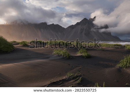 Sunset light filtering through clouds over black sand dunes and Vestrahorn mountain range at Stokksnes - Iceland
