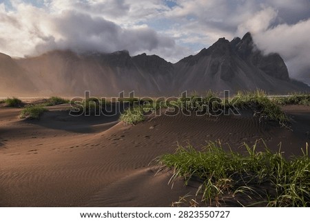 Sunset light filtering through clouds over black sand dunes and Vestrahorn mountain range at Stokksnes - Iceland