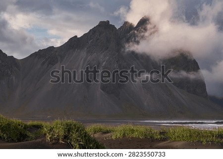 Sunset light filtering through clouds over black sand dunes and Vestrahorn mountain range at Stokksnes - Iceland