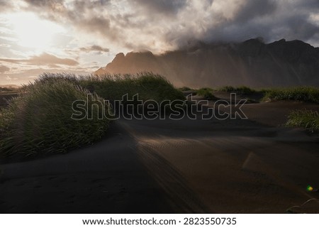 Sunset light filtering through clouds over black sand dunes and Vestrahorn mountain range at Stokksnes - Iceland