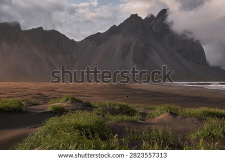 Sunset light filtering through clouds over black sand dunes and Vestrahorn mountain range at Stokksnes - Iceland