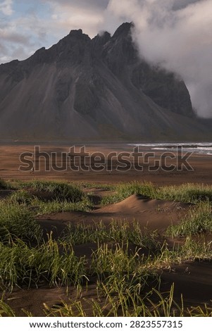 Sunset light filtering through clouds over black sand dunes and Vestrahorn mountain range at Stokksnes - Iceland