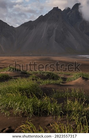 Sunset light filtering through clouds over black sand dunes and Vestrahorn mountain range at Stokksnes - Iceland