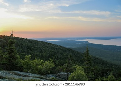 Sunset light over forested mountains and distant coastline viewed from Cadillac Mountain in Acadia National Park