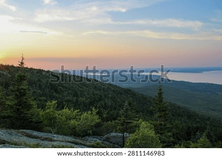 Sunset light over forested mountains and distant coastline viewed from Cadillac Mountain in Acadia National Park