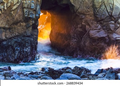 Sunset light rays pass through natural rock arch with crashing waves