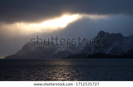 Sunset Lit Sky Over Foreboding Mountain Island with Ominous Clouds