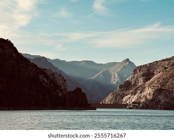 Sunset mountain landscape with serene lake, rugged cliffs, and a distant dam under a clear sky. Perfect for travel and nature themes. - Powered by Shutterstock