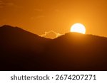 Sunset Mountains Orange: Sun sets behind silhouetted hills at dusk creating warm orange sky because of atmospheric effect.