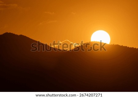 Sunset Mountains Orange: Sun sets behind silhouetted hills at dusk creating warm orange sky because of atmospheric effect.