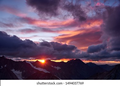 Sunset in mountains. Reflection of red sun on mountain snow peaks and clouds. Altai, Belukha area.