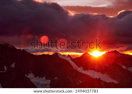 Sunset in mountains. Reflection of red sun on mountain snow peaks and clouds. Altai, Belukha area.