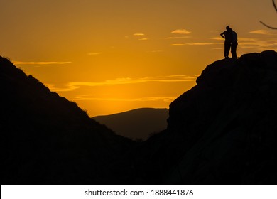 Sunset in the mountains. a young couple in love a guy and a girl stand on the top of the mountain during sunset, people silhouettes.