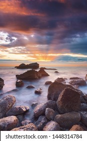 Sunset at natural pebble beach with light ways comes out between colorful clouds  - Shutterstock ID 1448314784