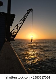 A Sunset Near The Ocean. A Crain Is Emerging From The Left To The Center.