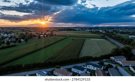 A sunset occurs over fields and mobile, manufactured homes in a rural area. The sky shows clouds colors as the sun sets in the evening. The layout includes farmland and roadways with buildings nearby.