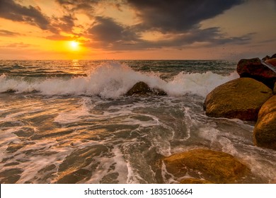 A Sunset Ocean Wave is Breaking on the Sea Shore with the Sun Setting on the Ocean Horizon